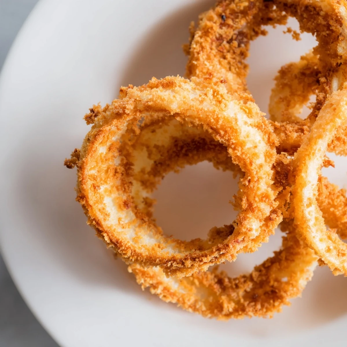 Crispy golden onion rings coated in light batter are served hot on a rustic platter for an irresistible appetizer snack. 
