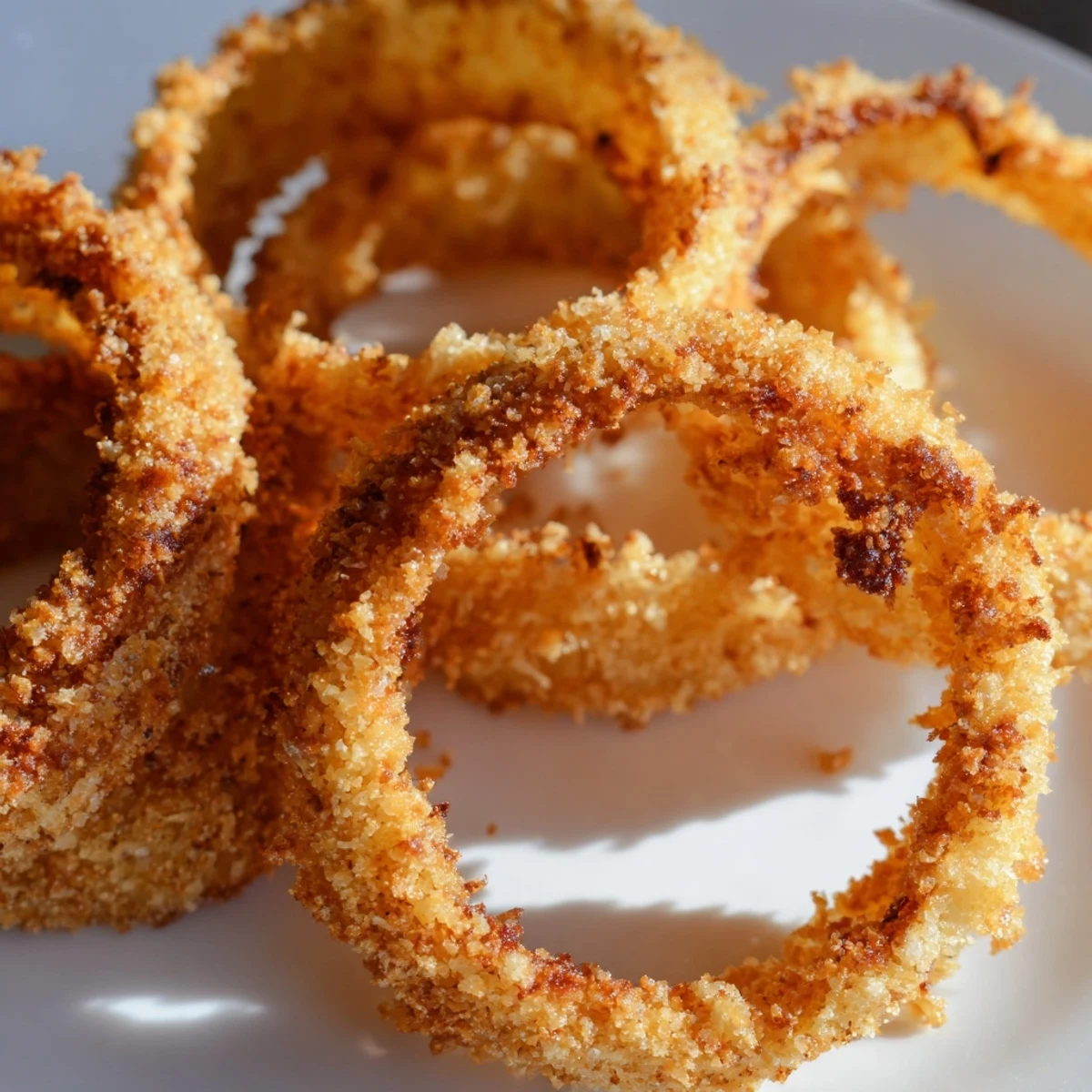 Piled high on parchment paper, golden-brown onion rings are ready to dip into ketchup or ranch on a kitchen counter.