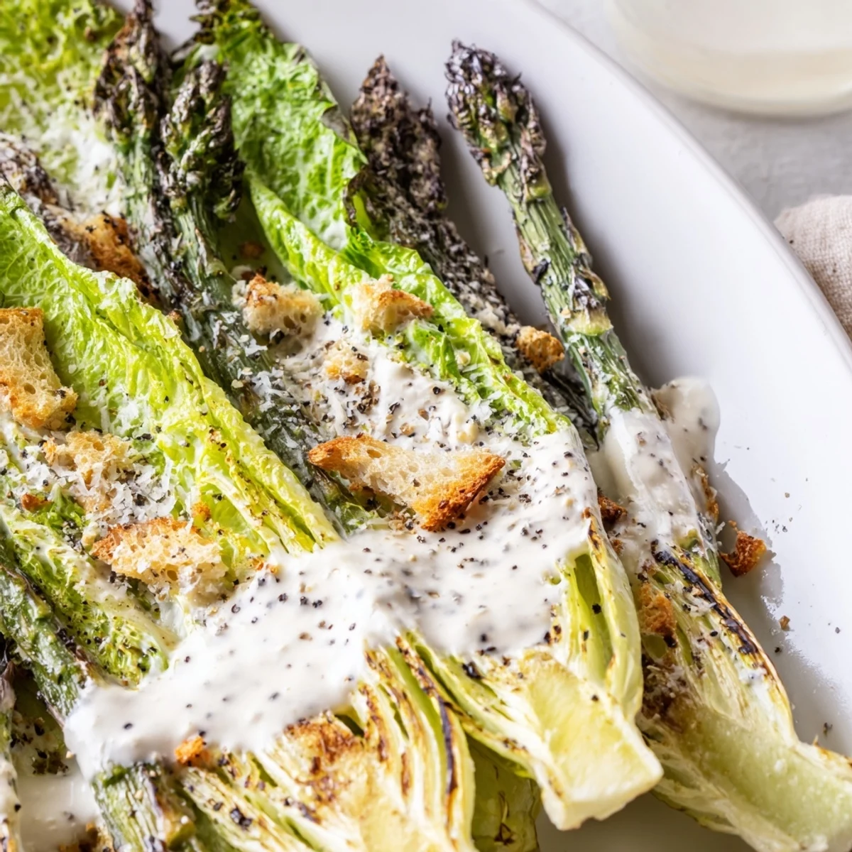 Sliced charred asparagus and shaved Parmesan create texture and flavor in this vibrant Roasted Asparagus Caesar Salad on a white plate.