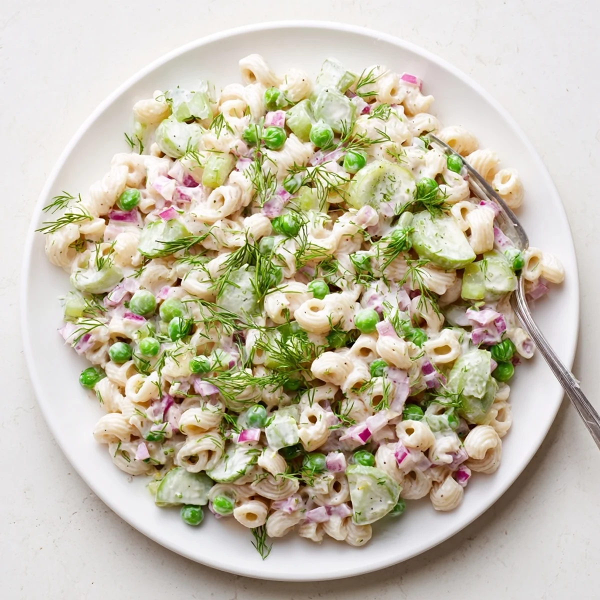Creamy Dill Pickle Pasta Salad is served in a white bowl, garnished with fresh dill and pepper.  