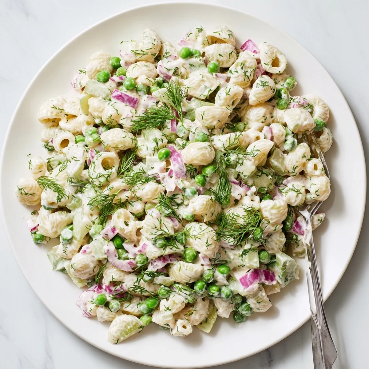 A close-up of Creamy Dill Pickle Pasta Salad with ditalini, peas, and diced pickles in a zesty dressing.  