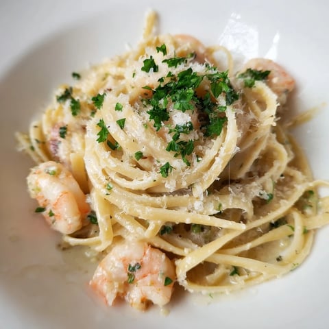 A close-up of Creamy Garlic Shrimp Pasta on a white plate, with linguine coated in a luscious, creamy garlic sauce and plump pink shrimp, garnished with fresh parsley and lemon wedges.