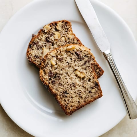 A rustic loaf of Banana Bread studded with chopped walnuts, resting on a wooden cutting board for a warm, homestyle feel.
