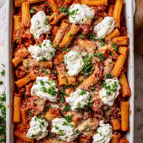 A close-up of Baked Ziti reveals layers of rich tomato sauce, melted cheese, and fresh parsley garnish.