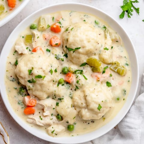 Spoonfuls of steaming Chicken and Dumplings reveal velvety broth and chunky vegetables, garnished with fresh parsley for a cozy dinner.