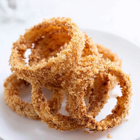 A close-up of deep-fried onion rings reveals crunchy textures and steam rising above a simple white serving plate. 