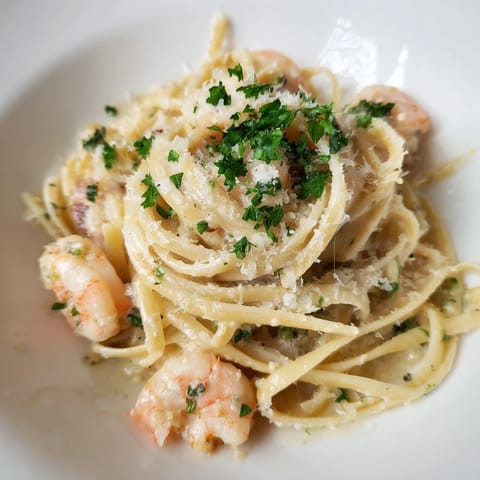A close-up of Creamy Garlic Shrimp Pasta on a white plate, with linguine coated in a luscious, creamy garlic sauce and plump pink shrimp, garnished with fresh parsley and lemon wedges.