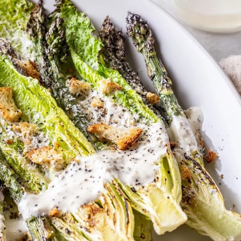 Sliced charred asparagus and shaved Parmesan create texture and flavor in this vibrant Roasted Asparagus Caesar Salad on a white plate.