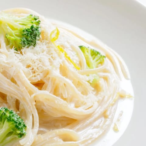 Close-up of One-Pot Lemon Broccoli Pasta with bright lemon zest, grated Parmesan, and fresh basil leaves for a vibrant, spring-inspired serving suggestion.  
