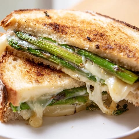 A close-up view of the Asparagus & Brie Grilled Cheese, showcasing gooey cheese oozing from buttery, toasted bread layers.