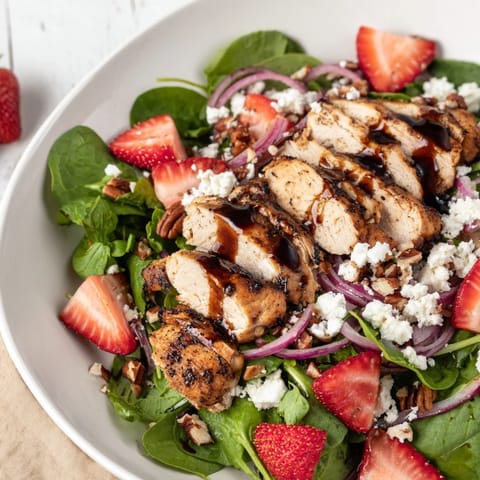 Freshly grilled chicken slices rest on crisp greens with juicy strawberries and crumbled feta, all drizzled with a glossy balsamic glaze.