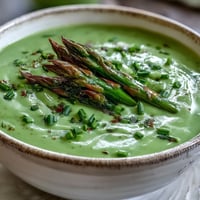 A bowl of creamy asparagus soup garnished with fresh chives and tender asparagus tips, served warm and ready to enjoy.