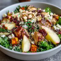 A vibrant Harvest Bowl featuring roasted sweet potatoes, sliced chicken, wild rice, kale, sliced almonds, and crumbled goat cheese on a white plate.