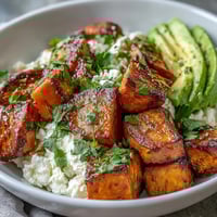 Roasted sweet potato cubes with crispy edges are arranged with creamy avocado and cottage cheese in a warm bowl. A spicy-sweet hot honey drizzle glistens over the top, ready to enjoy.